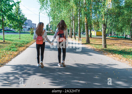 Jugendmädchen in Pullover, Blick nach hinten, Spaziergang mit Rucksäcken hinter, Sommer im Herbst und Frühjahr in der Stadt, am Wochenende nach der Schule. Hintergrund Bäume Stockfoto