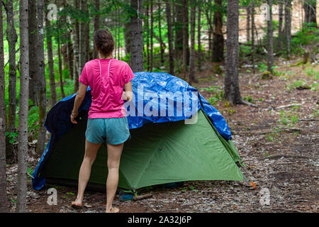 Eine schlanke kaukasische Frau ist von hinten gesehen, trägt einen rosa t-shirt, während die Errichtung einer Hütte in einer Waldlichtung auf einem Campingplatz zu Spiritualität gewidmet. Stockfoto