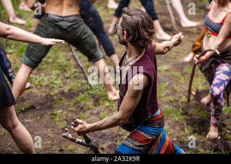 Eine bunte Kerl ist von der Seite üben alte kulturelle Übungen unter einer gemischten Gruppe von Menschen während einer multikulturellen Festival in der Natur gesehen. Stockfoto