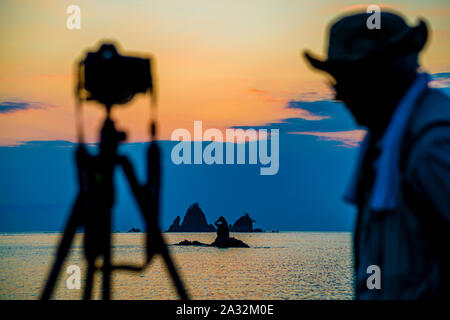 Am Strand von Tago Bay nehmen unzählige Sonnenuntergangsfotografen am Abend ihre Positionen ein und warten auf den Moment, in dem der Sonnenball für einen kurzen Moment wie ein Edelstein in die natürliche und runde Felsenmulde gleitet Stockfoto