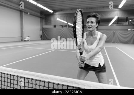 Reife Frau, schön spielen Tennis auf Innen- hof Stockfoto