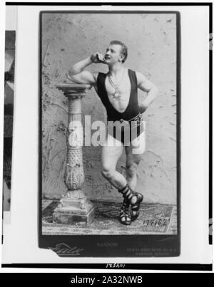 Eugene Sandow, full-length Portrait, stehen, lehnte sich auf Spalte nach links, das Tragen von Ringen leotard, Römische sandles, und sechs Stern Anhänger Stockfoto