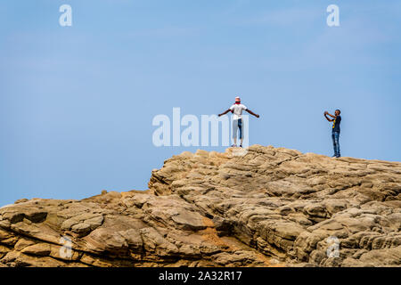Durban, Südafrika - 21. September 2019: Der junge Mann stand an der Spitze der Rock mit ausgestreckten Armen auf den Strand als sein Freund nimmt sein Foto. Stockfoto