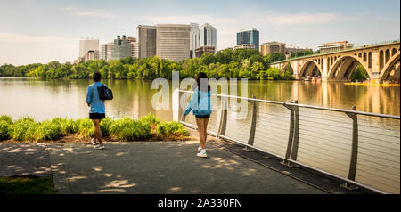 Zwei Frauen, die durch Fluss in blaue Mäntel mit Büro Gebäude im Hintergrund stehend Stockfoto