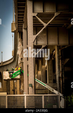 Zwei Arbeiter mit Schutzhelmen in einem Eimer an einer Brücke Stockfoto