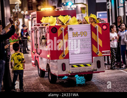 Ock Fire Engine beschleunigt die Stadt die Beantwortung einer mock Not thotough. Rolle spielende Kinder tragen gelbe Helme sitzen in den Rücken. Stockfoto
