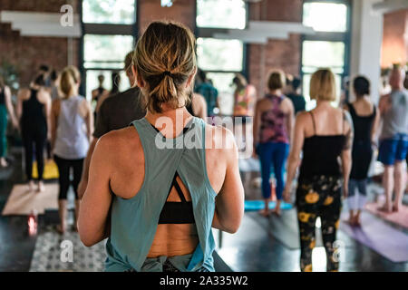 Einer weißen Frau mit ihrem Haar zurück gebunden ist, von hinten gesehen, in ein Gymnasium bei einer lokalen pilates Club. Blurry Menschen sind im Hintergrund gesehen. Stockfoto