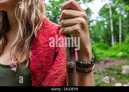 Eine Nahaufnahme auf dem Arm und Handgelenk eines jungen schamanische Mädchen mit langen blonden Haaren, das Tragen der Heiligen Gebetsperlen und halten einen langen Holzstab in der Natur. Stockfoto