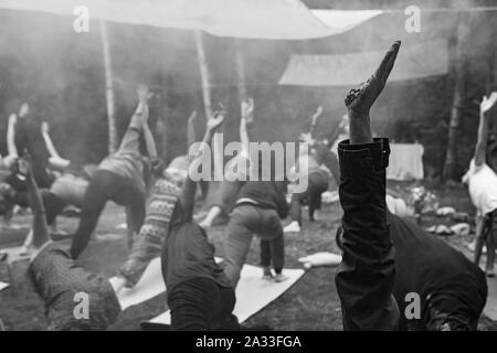 Eine atmosphärische Schwarz-Weiß-Ansicht auf eine multiethnische Gruppe von vernünftigen Menschen üben Yoga Posen in Wäldern während einer schamanischen Rückzug. Stockfoto