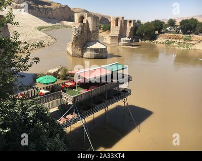 09. September 2019, in der Türkei, in Hasankeyf: Eine malerische Cafe und Jahrhunderte alten Brückenpfeiler sind auf den Tigris gelegen. Das Dorf liegt in einer einzigartigen Kulturlandschaft auf dem Tigris. Menschen haben sollte hier für rund 12.000 Jahre zu vereinbaren. Aber bald Hasankeyf wird unter Wasser von einem riesigen Stausee versinken. Etwa 70 Kilometer weiter flussabwärts, das Neue ilisu Megadam hat begonnen Arbeit und hat stauen Wasser seit mehreren Wochen. Nach Angaben der örtlichen Behörden, im Herzen der kleinen Stadt Zentrum ist von 8. Oktober evakuiert werden. Viele Häuser werden dann es abgerissen werden. Die Menschen Stockfoto