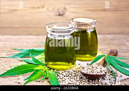 Hanf Öl in zwei Gläser mit Korn in einen Löffel und auf dem Tisch, Cannabis Blätter auf dem Hintergrund einer alten hölzernen Board Stockfoto