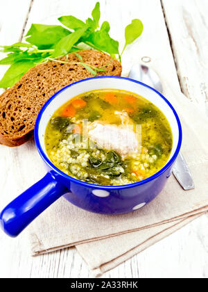 Schweinerippchen Suppe mit Couscous und Spinat in eine blaue Schale auf dem Handtuch, Brot auf Holzbrett Hintergrund Stockfoto