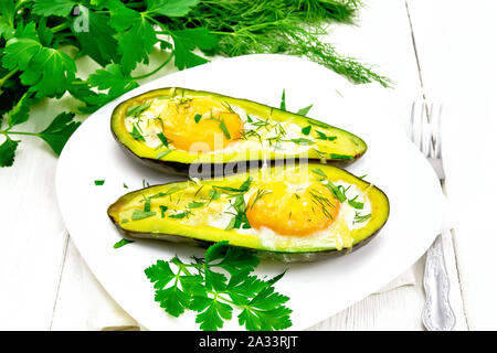 Rührei mit würzigen Grünen in zwei Hälften von Avocado in eine Platte auf Serviette, Gabel, Petersilie auf Holzbrett Hintergrund Stockfoto