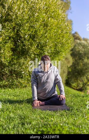 Man Yoga Asanas im City Park inspiriert. Fitness im Freien und Life Balance Konzept. Stockfoto