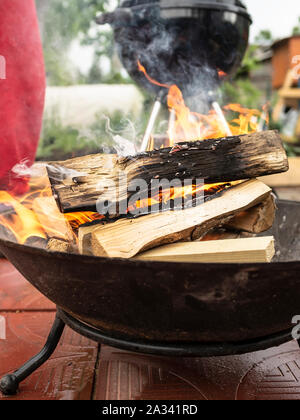 Holz Brennen im Lagerfeuer Schüssel die Kohlen für das Grillen und Barbecue vorzubereiten, bewölkten Sommertag in die Landschaft. Stockfoto