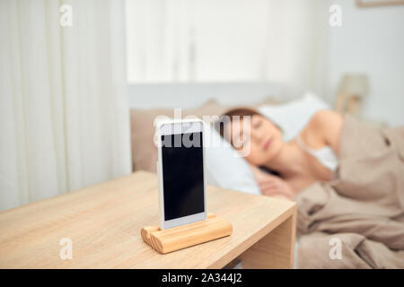 Asiatische Frau schlafend im Bett geweckt durch Alarm am Handy Stockfoto