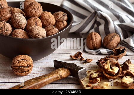 Knacken Walnüsse, rustikalen Herbst Konzept. Risse Walnüsse mit alten Hammer und braune Schale im Hintergrund. Nahaufnahme. Stockfoto