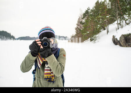 Eine Frau, die Fotografin in warme Kleidung und einen Rucksack auf dem Rücken hält eine Kamera in der Hand und nimmt Bilder der Winterlandschaft. Gegen th Stockfoto