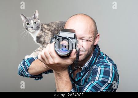 Süße Katze sitzt auf der Schulter des Fotografen, der hält einen alten Film der Kamera in der Hand. Close-up. Stockfoto