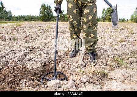 Der Mensch auf der Suche nach Schatz mit einem Metalldetektor und Spaten auf dem Feld, Sommertag. Stockfoto