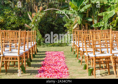 Runde Hochzeit arch im Boho style für eine Zeremonie mit frischem Grün und Blumen dekoriert. Tiffany Stühle und Rosa und Rot Blütenblatt Gang. Stockfoto