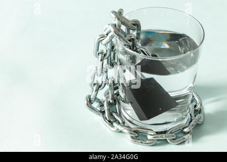 Ein Glas Wasser in einer Kette gewickelt und mit einem Vorhängeschloss. Das Konzept des Problem der kleinen Trinkwasser in der Welt. Für te Ort Stockfoto