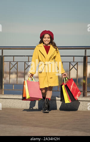 Stilvolle Unterbringung in französischen Baskenmütze und fallen Mantel. Herbst Trend. Shopping Tag. Happy kleines Mädchen. Kleines Mädchen mit Einkaufstüten. Wetter im Frühling. Kid Mode suchen. Angenehmes einkaufen. Erfolgreiche Geschäfte. Stockfoto