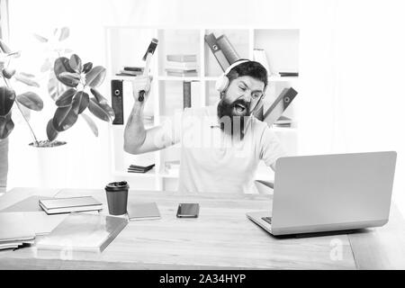 Hasse office Routine. Man bärtige Kerl Kopfhörer Büro schwingen Hammer auf dem Computer. Langsame Internetverbindung. Veraltete Software. Computer lag. Gründe für Computer zurückbleiben. Wie fix langsam hinterher. Stockfoto
