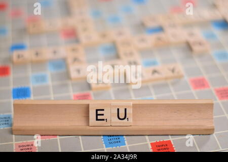Der Name "EU" (Europäische Union) in Holz- Scrabble Fliesen auf einem Baugruppenträger. Hintergrund ist ein Vintage board, unscharf, mit kopieren. Stockfoto