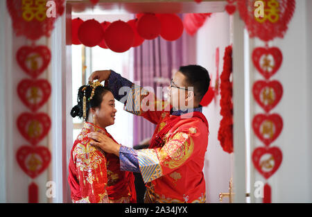 (191005) - TONGREN, Oktober 5, 2019 (Xinhua) - Bräutigam Pan Rongdong (R) Ordnet headwear für Braut Tan Lifei am Tag ihrer Hochzeit in ihrem Haus im Stadtteil Bijiang Tongren Stadt, im Südwesten Chinas Provinz Guizhou, Oktober 4, 2019. Pan Rongdong ist Mitarbeiterin in der mütterlichen und Kinder Gesundheit Service Center in Wanshan Kreis Tongren. Im September 2017, wenn die Pfanne zu Wengbei Dorf Aozhai Gemeinde versandt wurde in Wanshan auf die Verringerung der Armut zu arbeiten, erhielt er mit Tan Lifei, Direktor der anti-Armut station für Aozhai kennen. Bei der Arbeit an Ziel Stockfoto