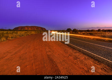 Auto Licht Wanderwege entlang der Straße nach Uluru Ayers Rock in der Nacht. Die riesigen Monolith aus Sandstein Symbol des australischen Outback Red Centre im Uluru-Kata Tjuta Stockfoto