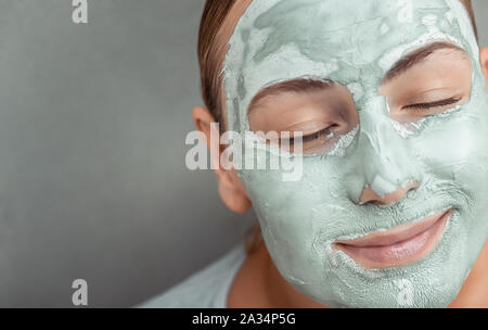 Closeup Portrait von einer schönen Frau mit blauen Ton Maske auf Gesicht, Anti Akne oder Anti age Kur, gesunde Haut, grauer Hintergrund Stockfoto