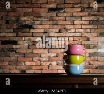 Bunte tiffin Carrier auf Holzschrank mit unscharfen Vintage brick wall gegen warmes Licht Stockfoto