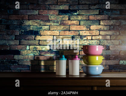 Bunte tiffin Träger und Plastikflaschen auf Holzschrank mit Vintage Mauer Hintergrund gegen warmes Licht Stockfoto