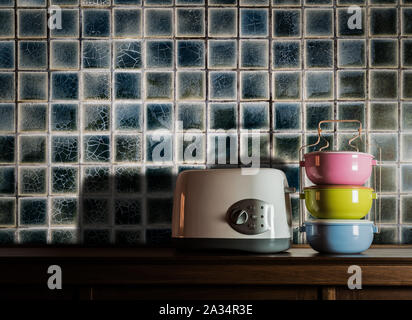 Bunte tiffin Träger und Toaster auf Holz Schrank in der Küche Zimmer gegen warmes Licht Stockfoto