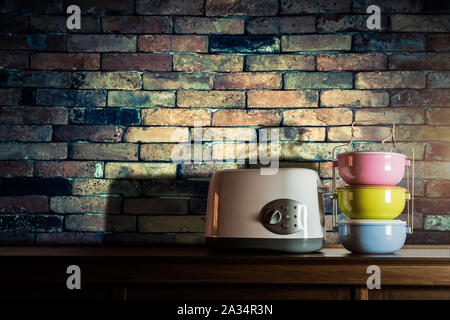 Bunte tiffin Träger und Toaster auf Holzschrank mit Vintage Mauer Hintergrund gegen warmes Licht Stockfoto