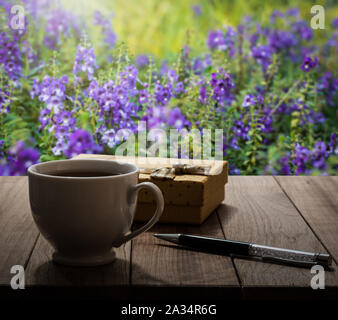 Kaffee, Stift und Geschenkbox auf hölzernen Tisch im Garten unter Sonnenlicht Stockfoto