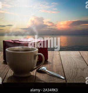 Heißer Kaffee und Geschenkbox auf Holztisch mit Marine unter Sonnenlicht Stockfoto