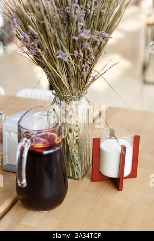 Sommer hausgemachte Dunkelrot Limonade mit frischen in Scheiben geschnittenen Zitronen in einer Kanne auf hölzernen Tisch. getrocknete Blumen Hintergrund Bouquet. Sonnigen Tag verschwommenen Hintergrund Stockfoto