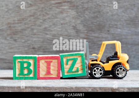 Spielzeug Gabelstapler halten schreiben Block Z zu Wort vervollständigen Biz (Abkürzung) auf Holz Hintergrund Stockfoto