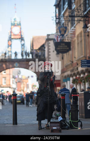 Esme Marie Sallnow, ein Straßenmusikant in einem 1920 gekleidet s Kostüm unterhält Shopper in Chester Stadtzentrum. Hinter ihr der ikonischen Eastgate Town Clock. Stockfoto