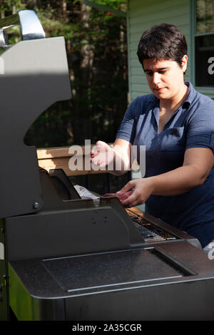 Frau setzt ein Stück Hamburger auf den Grill an einem sommerlichen Abend Stockfoto