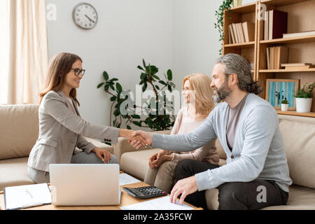 Casual bärtiger Mann zitternden Hand der jungen weiblichen real estate agent über Schreibtisch Stockfoto