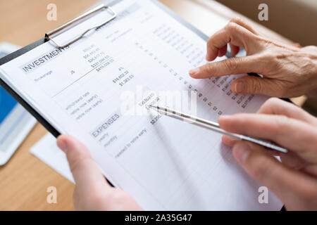 Menschliche Hand mit Stift auf Summe der Aufwendungen während der Diskussion Stockfoto