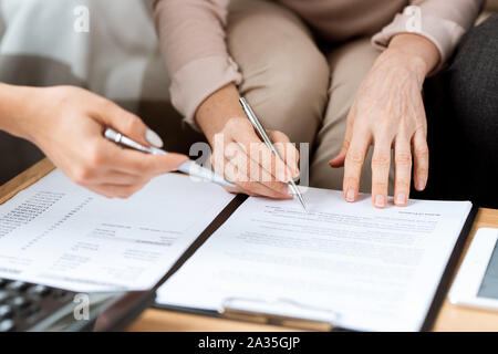 Hände von ausgereiften Client und Grundstücksmakler mit Kugelschreiber auf Vertrag zeigen Stockfoto