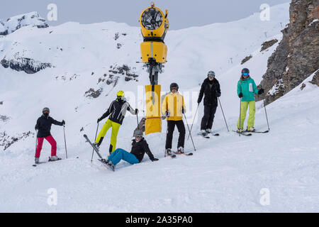 Junge Erwachsene im Winter, Schlange stehen am Hang das Tragen von Ski-, Snowboard-, Helm und Schutzbrille mit Schnee Berg im Hintergrund an einem bewölkten Tag.