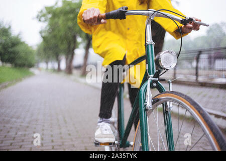 Fahrrad fahren im Regen. Nahaufnahme von Fahrrad Fahrer tragen gelbe Regenmantel Stockfoto