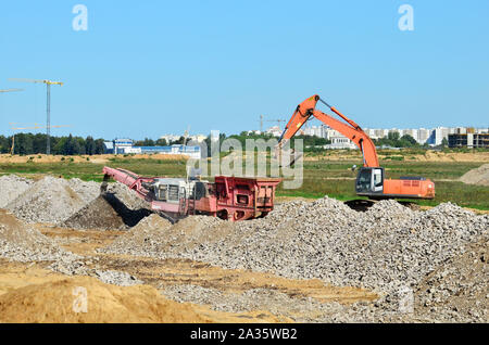 Schwerer Raupenbagger last Stein, mit alten Asphalt oder Beton Abfall in eine Mobile Backenbrecher Maschine. Die Zerkleinerung und Verarbeitung in Kies für Recycling Stockfoto