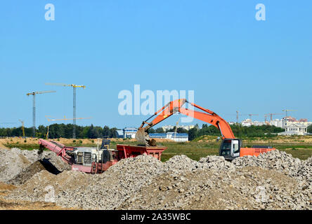 Schwerer Raupenbagger last Stein, mit alten Asphalt oder Beton Abfall in eine Mobile Backenbrecher Maschine. Die Zerkleinerung und Verarbeitung in Kies für Recycling Stockfoto