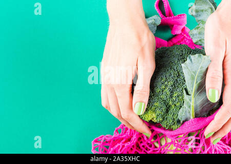 Null Abfall Konzept. Woman's Händen grüne Maniküre holding Rosa wiederverwendbare Tasche mit Brokkoli. Kunststoff freien Lebensstil Stockfoto